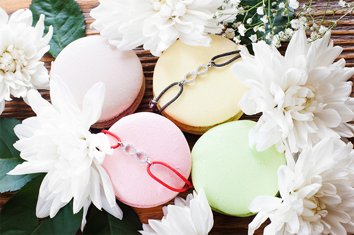 Macaroon french cookies with best friend bracelets. Pretty accessories with infinity sign pendants presented on colorful sweets in blossom frame, close-up